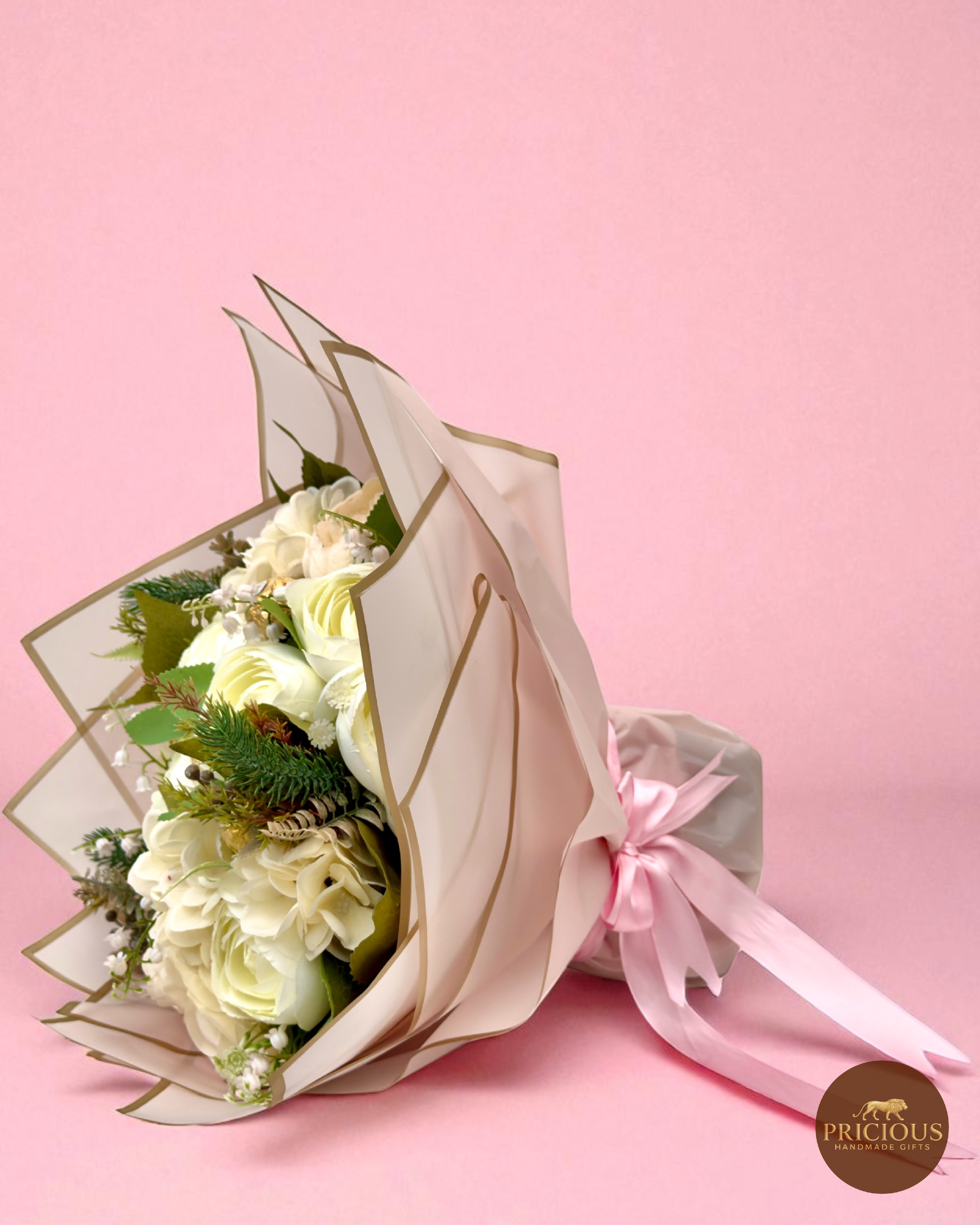 Ivory rose, peony and hydrangea chocolate bouquet with gold-wrapped Ferrero Rocher in champagne-edged wrap and pink ribbon on a pink backdrop.