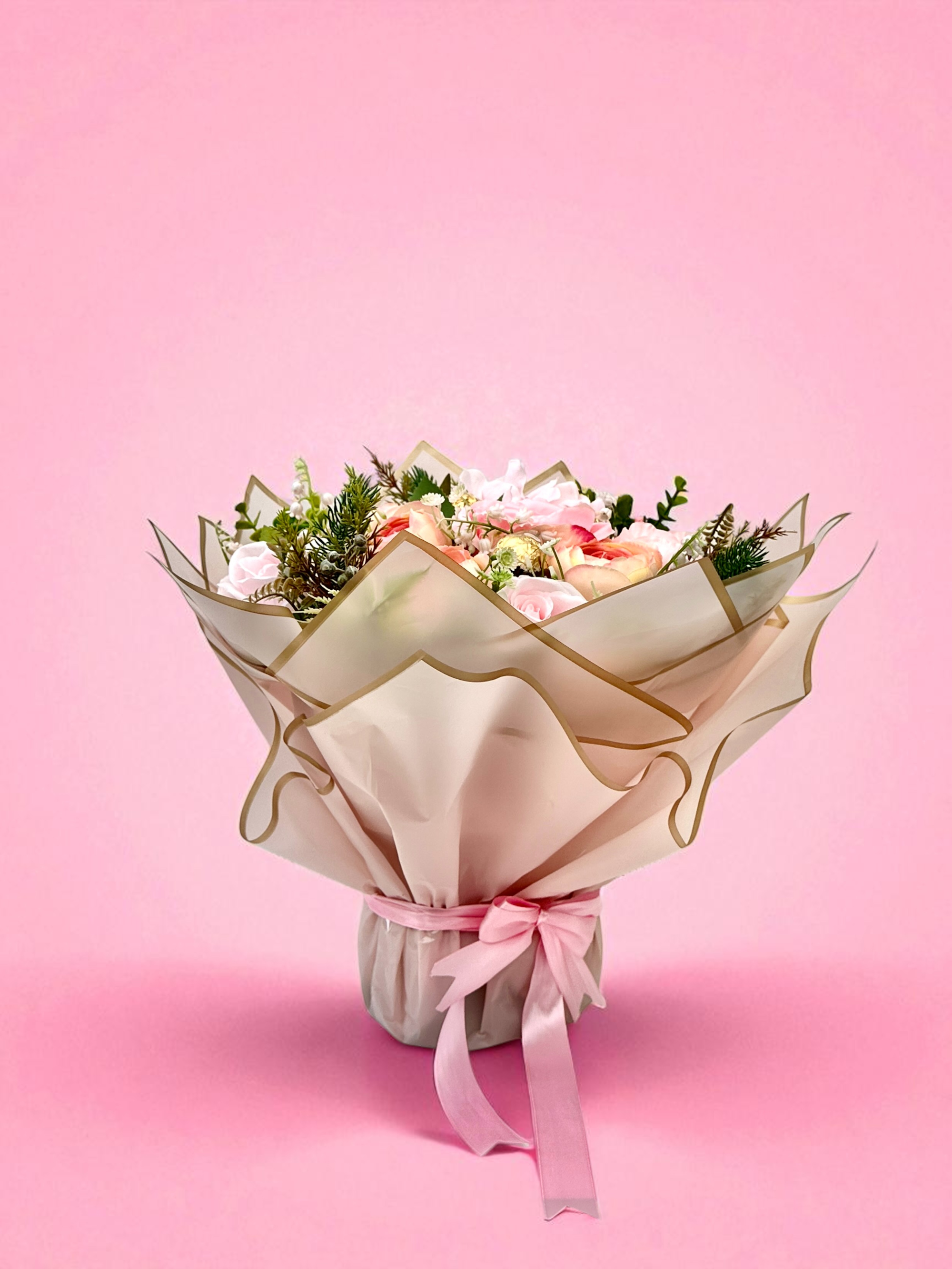 Bouquet of pink roses with chocolate candies wrapped in light pink paper and gold ribbon on a beige background