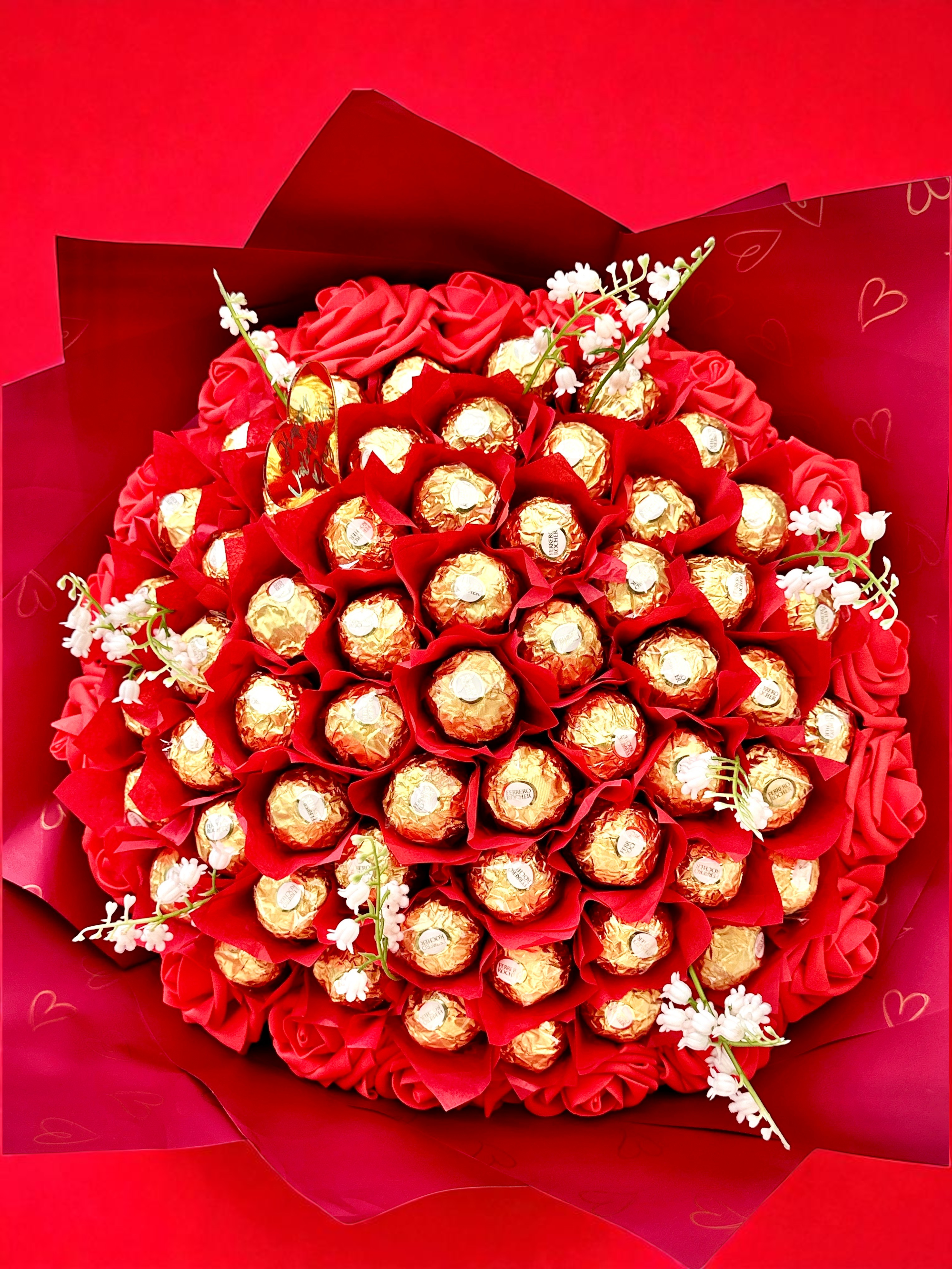 Bouquet of flowers and Ferrero Rocher chocolates wrapped in pink paper with a pink ribbon on a beige background.