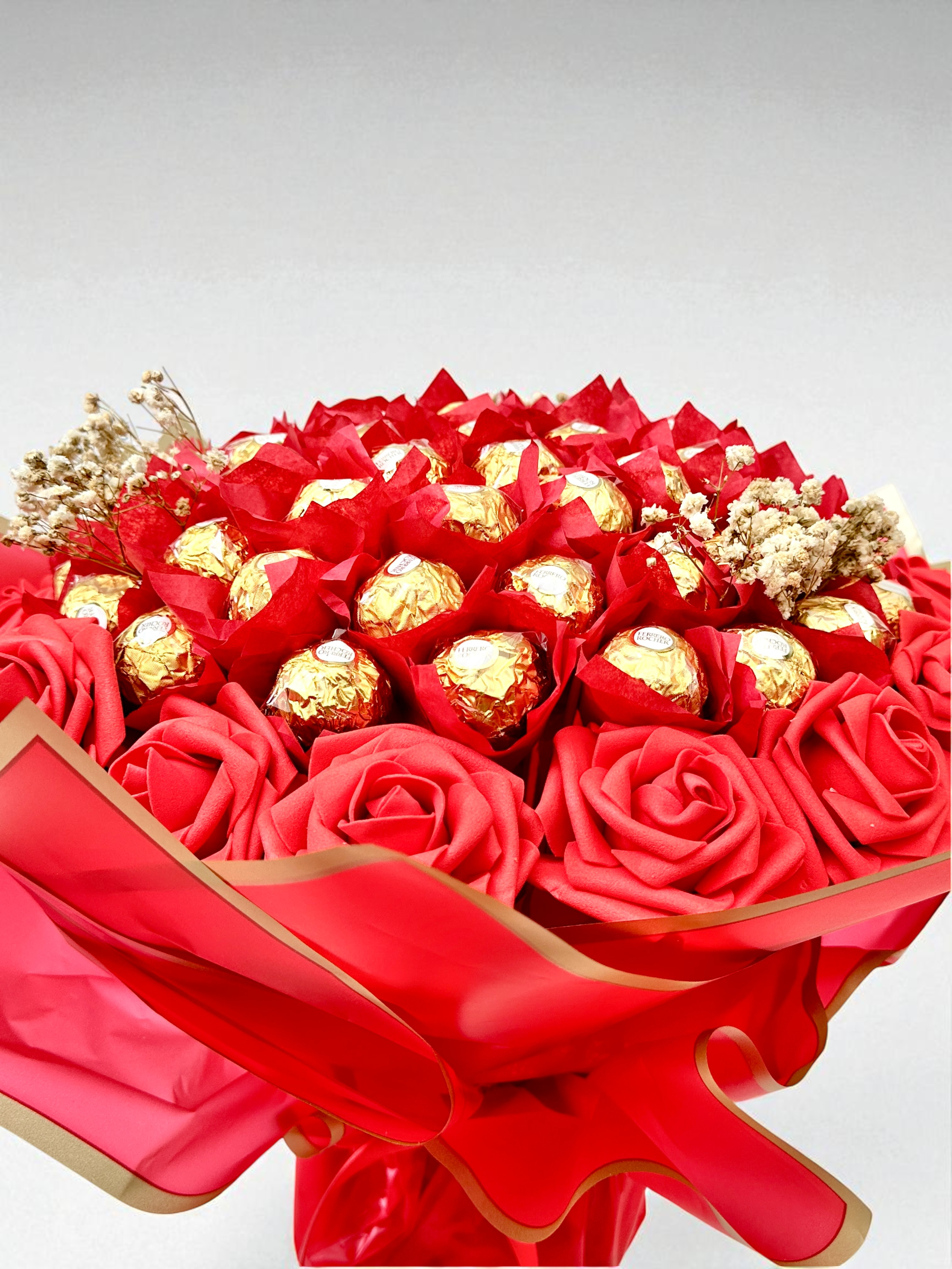 Bouquet of gold Ferrero Rocher chocolates wrapped in brown paper with a green ribbon on a beige background.