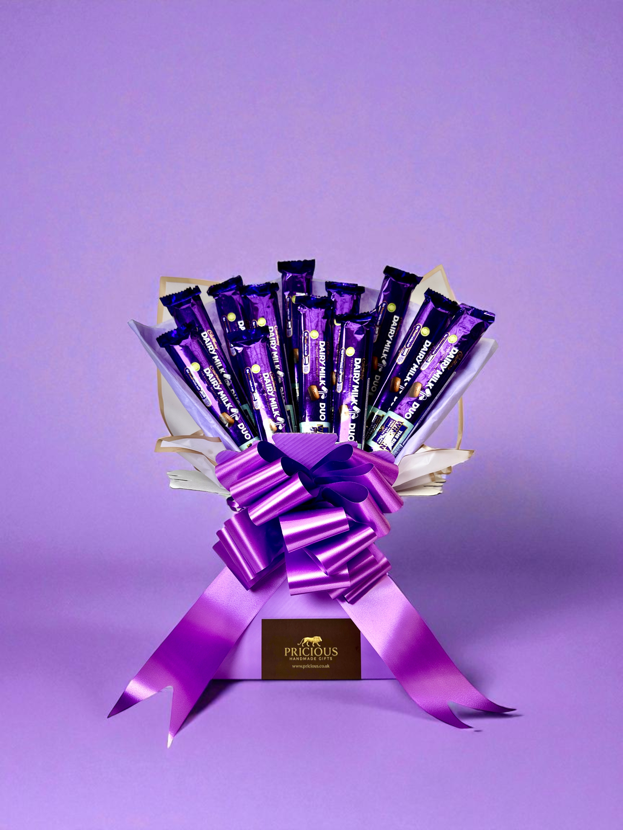 Three bouquets of Cadbury Dairy Milk chocolate bars with purple ribbons and flowers on a beige background.