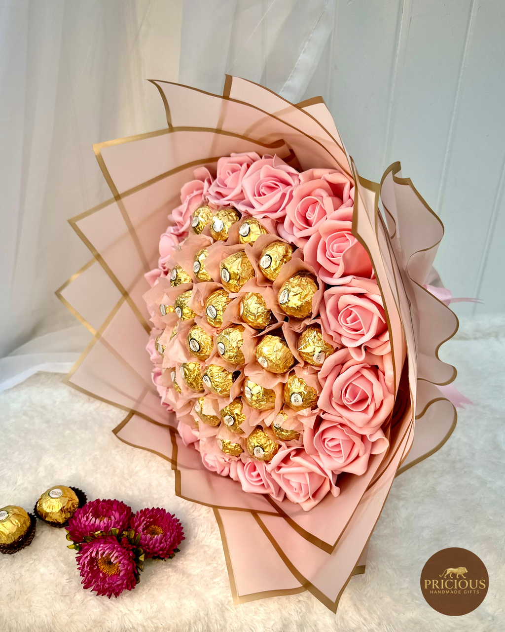 Bouquet of pink roses with gold chocolates wrapped in decorative paper, branded 'PRICIOUS'.