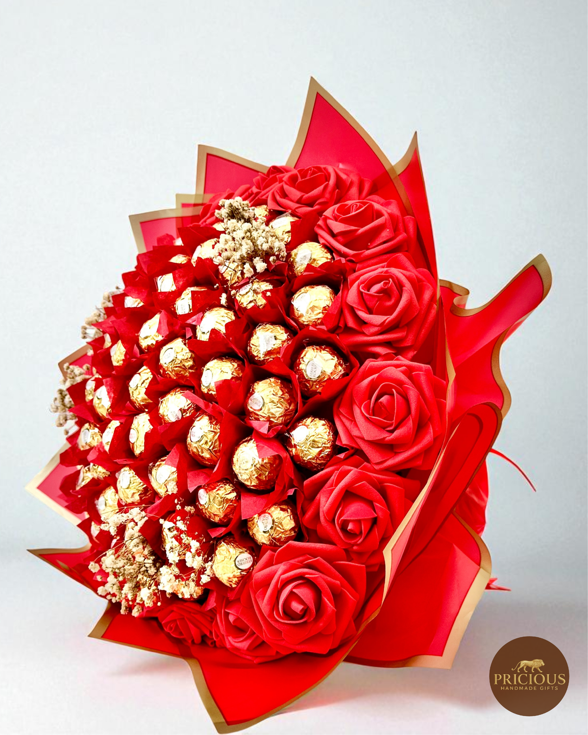 Bouquet of red roses and gold Ferrero Rocher chocolates wrapped in red paper with gold accents on a white background.