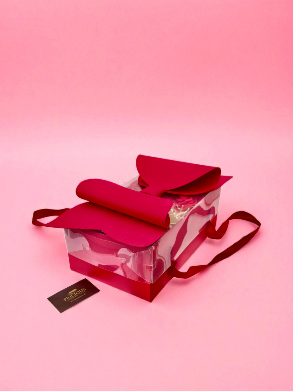 Red shoe in a clear box on a pink background with a visible brand label.