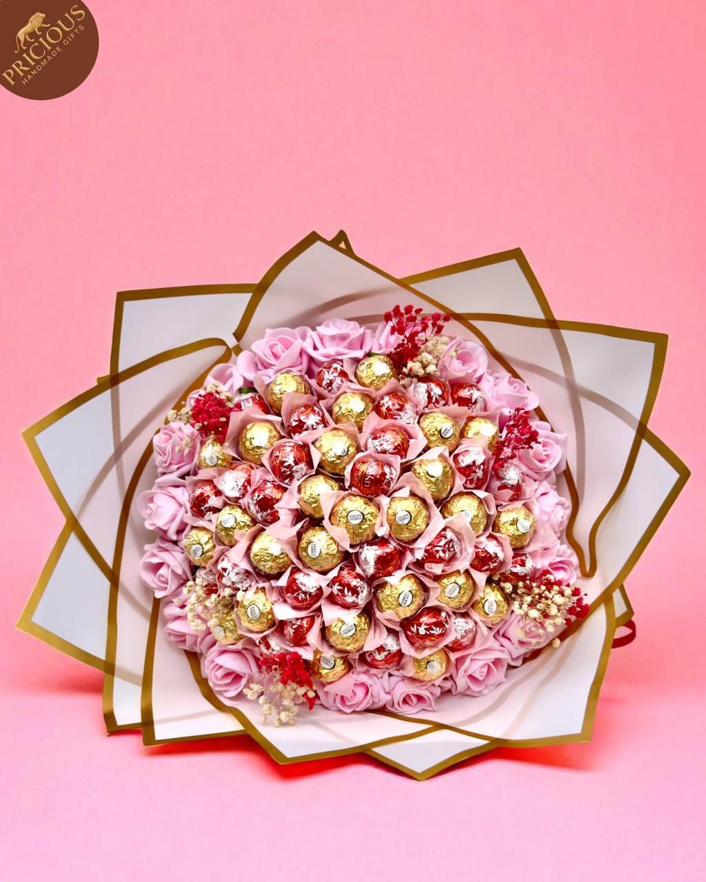 Overhead view of mixed Ferrero Rocher and Lindt Lindor bouquet among pink artificial roses.