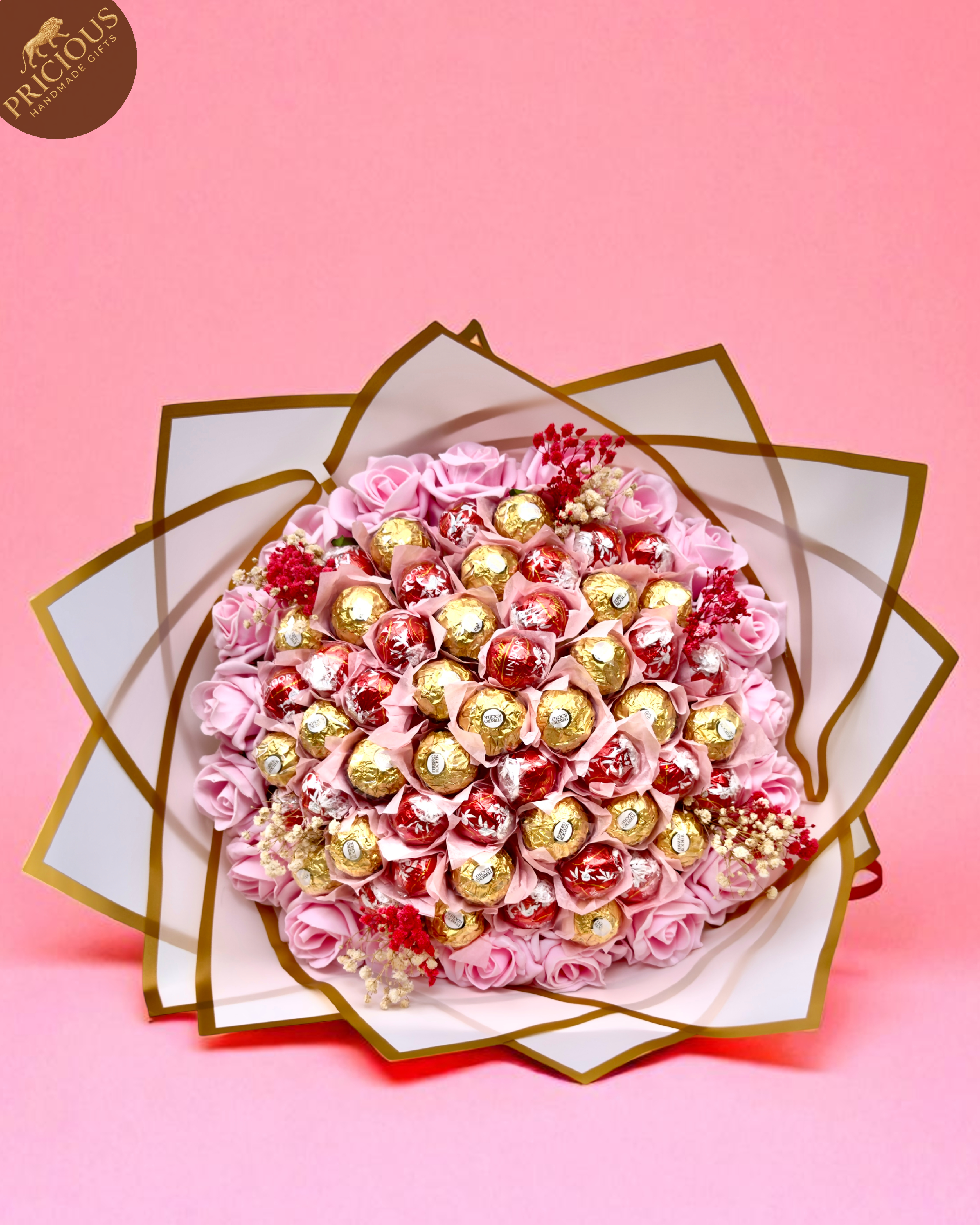 Overhead view of mixed Ferrero Rocher and Lindt Lindor bouquet among pink artificial roses.