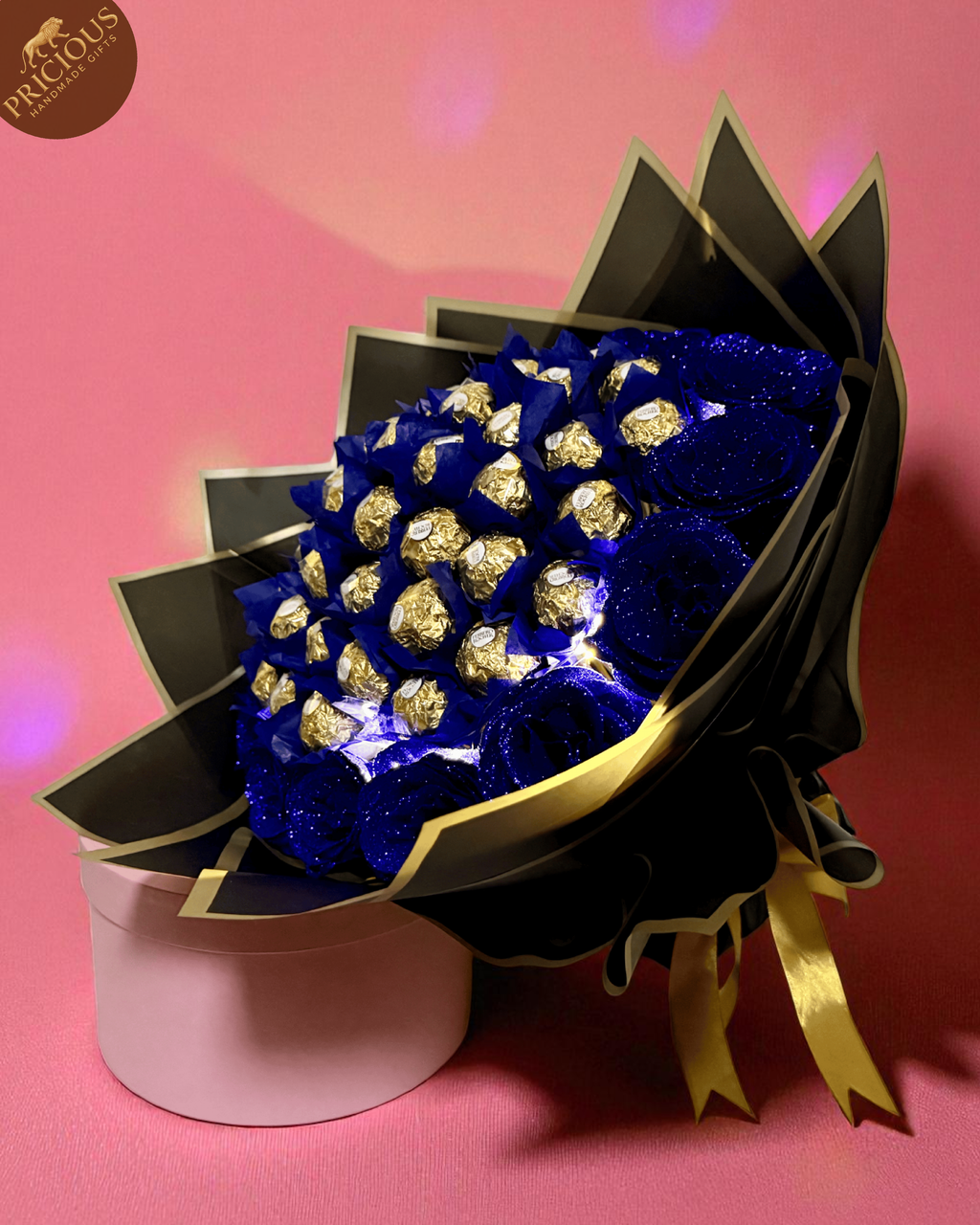 Hand-tied Ferrero Rocher bouquet with LED lights and glitter-blue artificial roses, black & gold wrap (angled view).