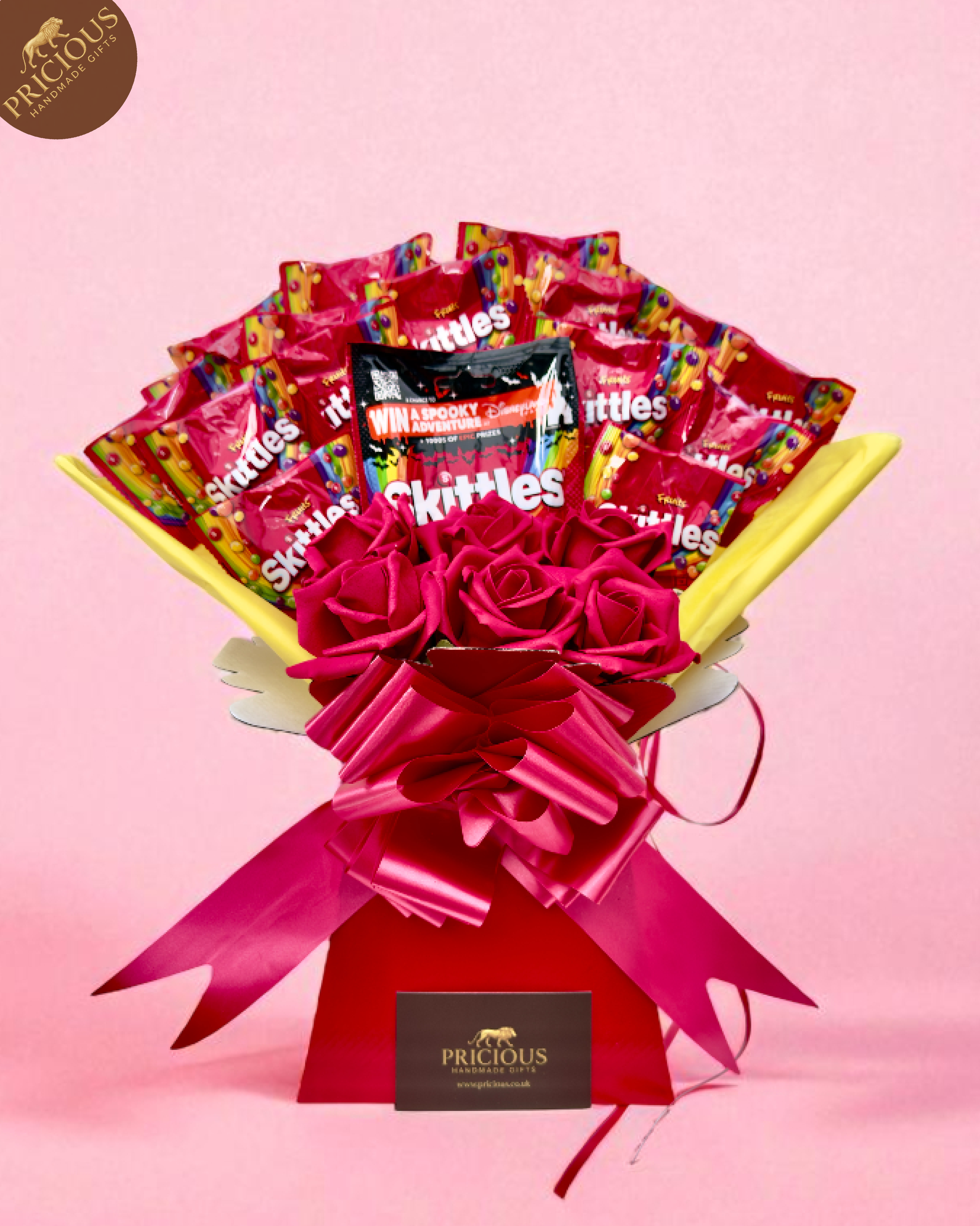 Hand-tied Skittles sweets bouquet box with artificial pink roses and yellow wrap.