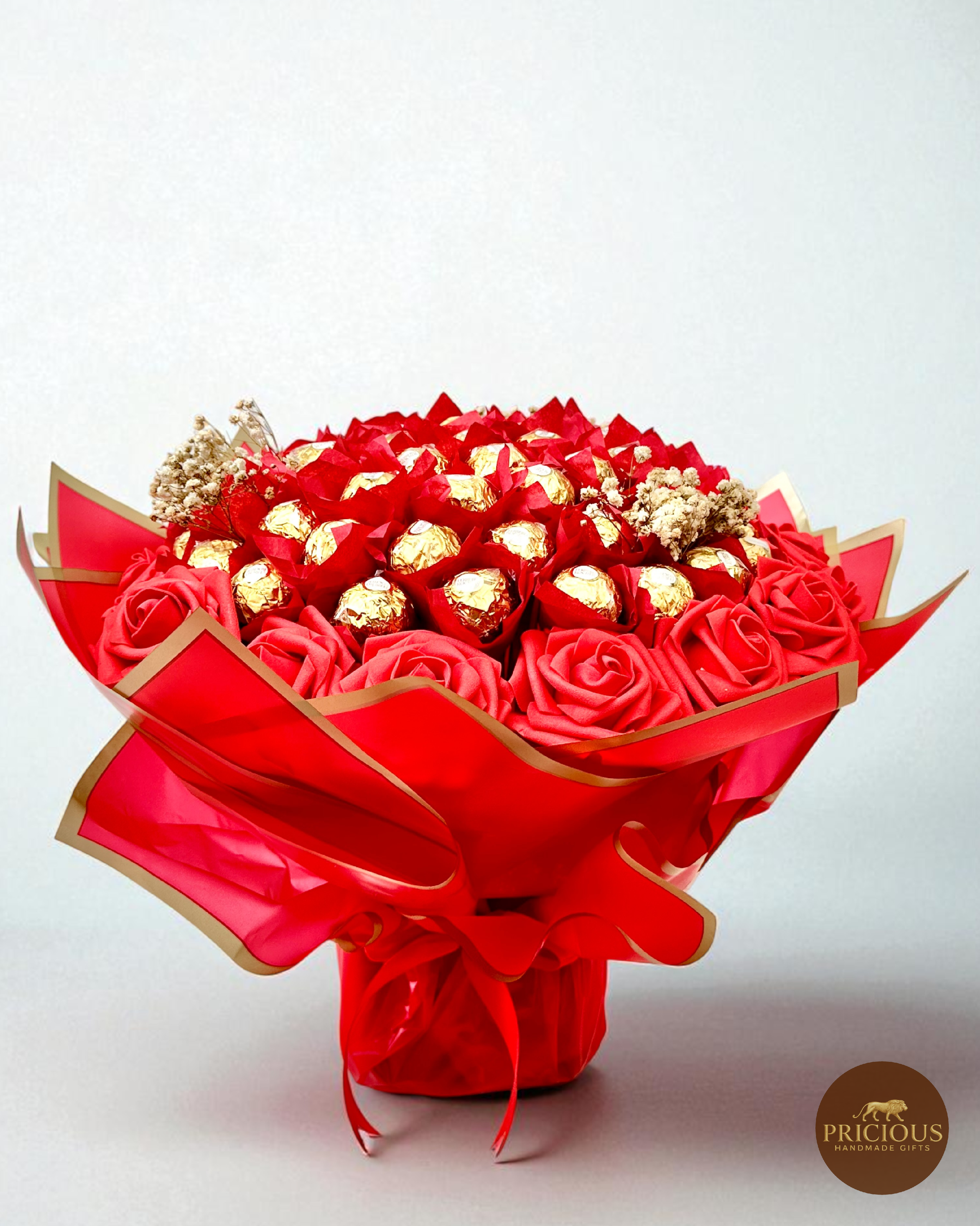Bouquet of red roses and gold Ferrero Rocher chocolates wrapped in red paper with gold accents on a white background.