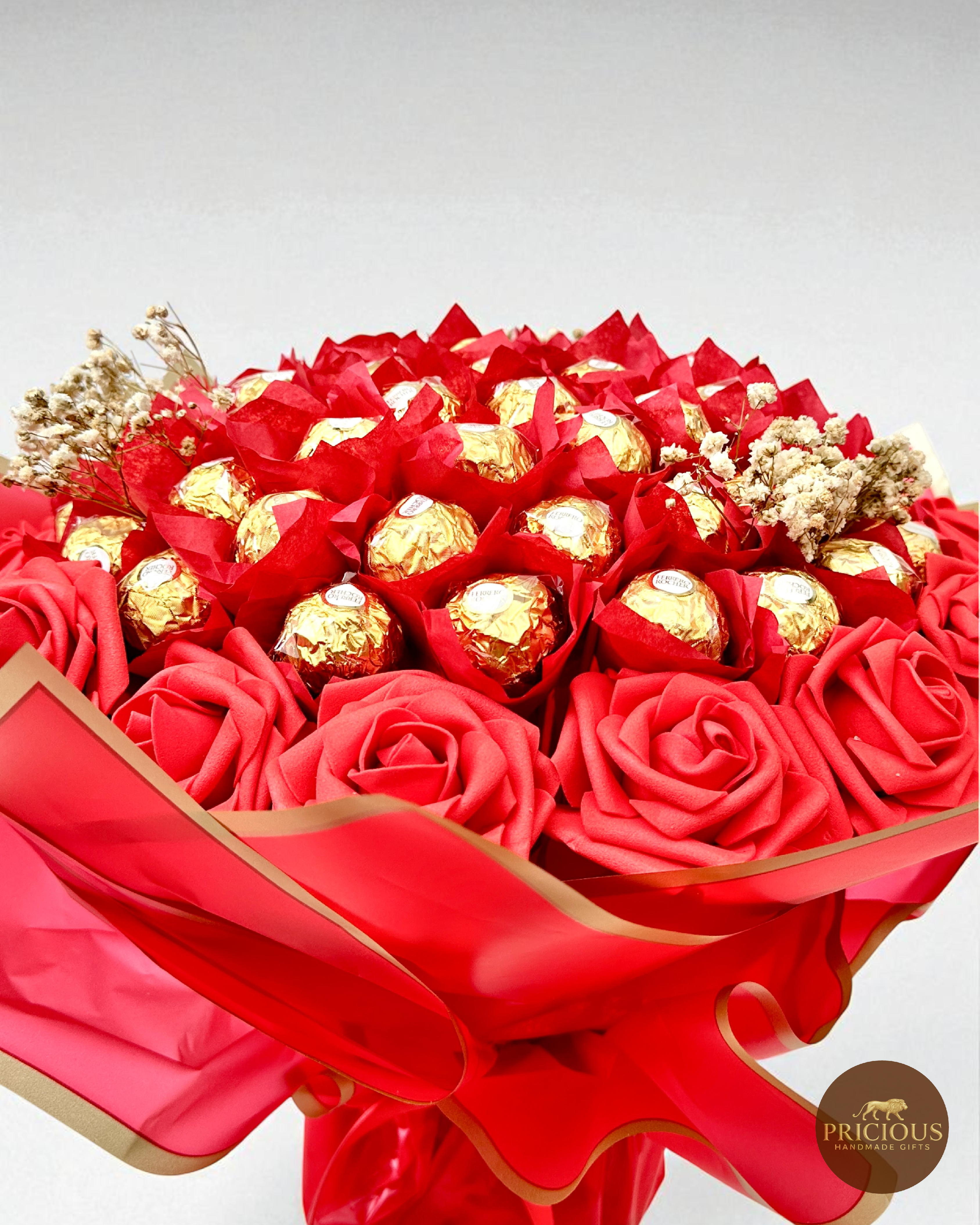 Bouquet of red roses and gold-wrapped chocolates with a red ribbon on a light gray background.