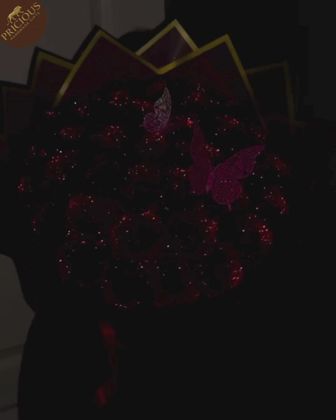 Top view of red glitter artificial roses hand-tied bouquet, butterfly accents, pink hat box display.